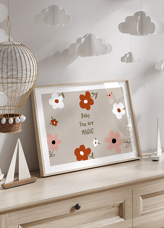 Een ingelijste print met een bloemmotief en de tekst "Baby You are Magic" wordt uitgestald op een houten dressoir, met daarboven een decoratieve papieren lantaarn.