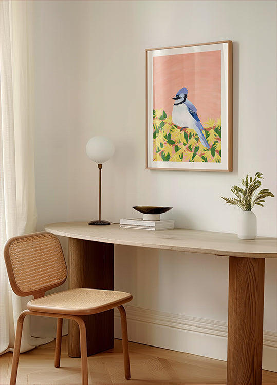 een gezellig hoekje van een kamer met een houten bureau, een geweven stoel, een lamp en een ingelijste afbeelding van een blauwe vogel op een gele achtergrond.