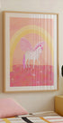 een ingelijste poster van een eenhoorn met een roze en wit kleurenschema, tegen een roze en gele achtergrond met een regenboogboog.