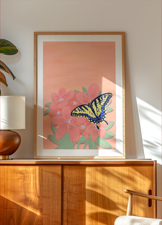 een ingelijst schilderij van een vlinder op een roze bloem, tentoongesteld op een houten kast of plank.