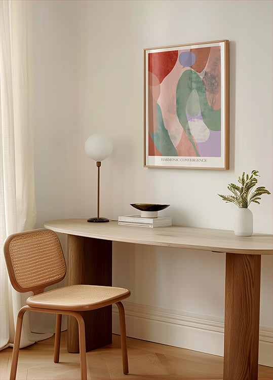 een minimalistische werkruimte met een houten bureau, een geweven stoel, een lamp en een ingelijst abstract schilderij aan de muur.