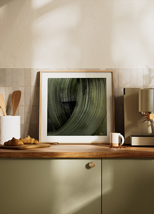 een ingelijste foto van een groen blad op een aanrecht, met op de achtergrond een koffiezetapparaat en andere keukenartikelen zichtbaar.