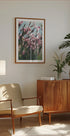 een gezellige woonkamer met een houten kast, een beige fauteuil, een ingelijste foto van roze bloemen en een potplant.