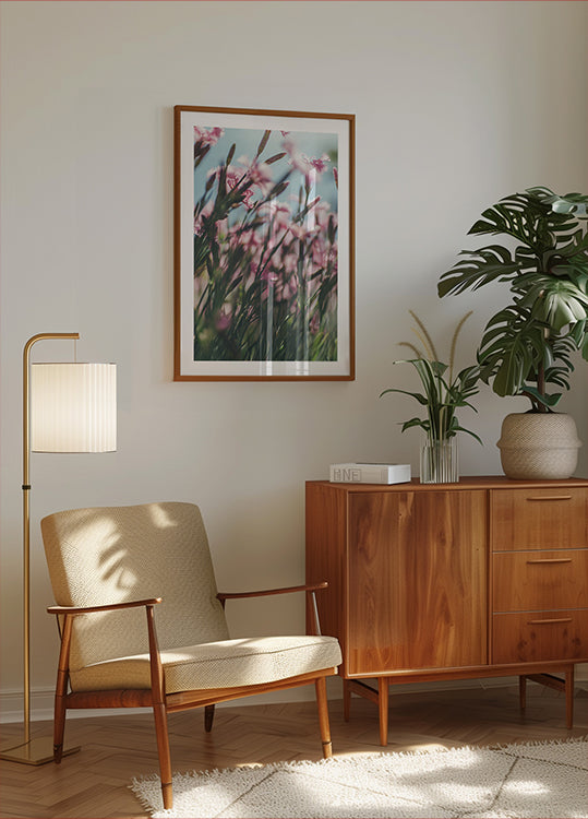 een gezellige woonkamer met een houten kast, een beige fauteuil, een ingelijste foto van roze bloemen en een potplant.