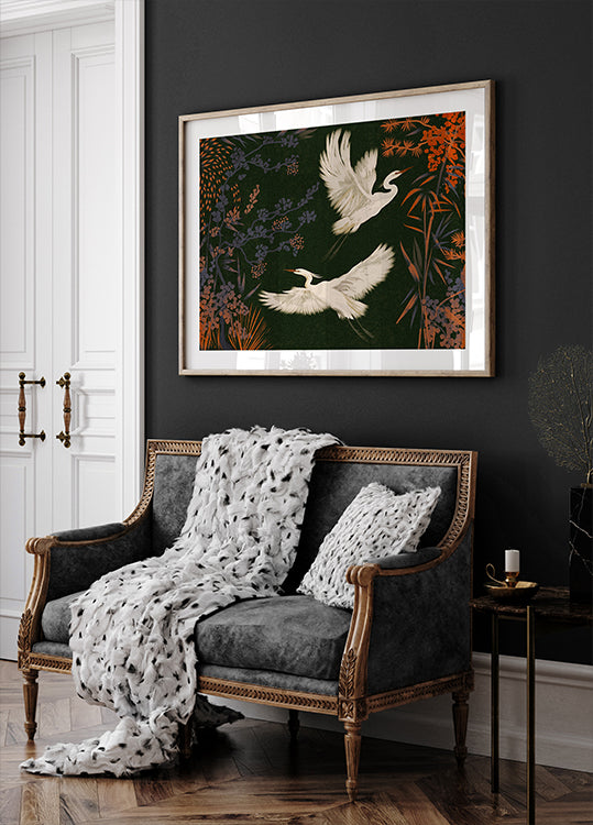 een zwart-witte bank met een witte deken en twee witte kussens, tegen een donkere muur met daarboven een ingelijst schilderij van twee witte vogels in vlucht.