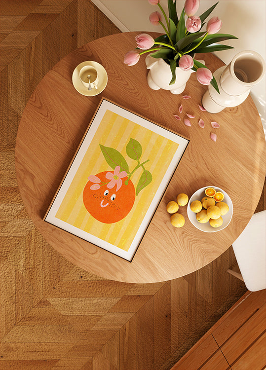 een houten tafel met een ingelijste afbeelding van een sinaasappel, een schaal met citroenen, een vaas met roze tulpen en een kaars erop.