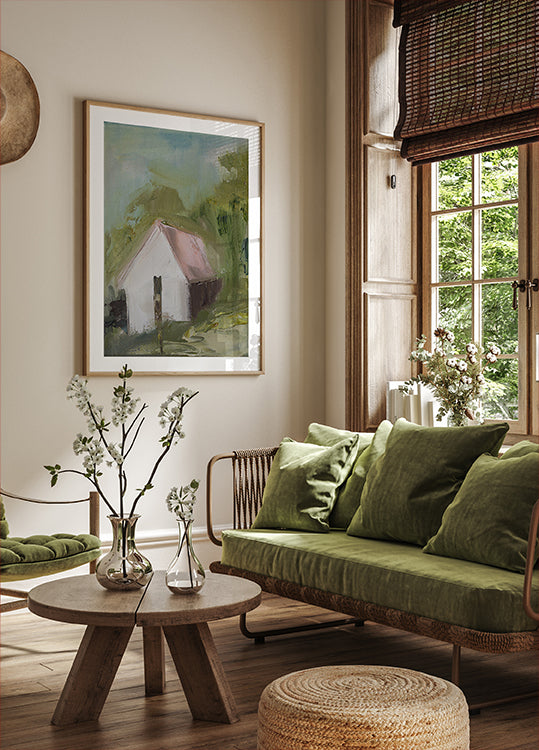 een gezellige woonkamer met een groot raam, een groene bank, een houten salontafel en een ingelijst schilderij van een huis.