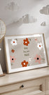 Een ingelijste print met een bloemmotief en de tekst "Baby You are Magic" wordt uitgestald op een houten dressoir, met daarboven een decoratieve papieren lantaarn.